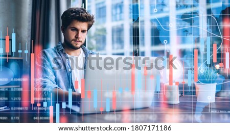 Young man working at modern office.Technical price graph and indicator, red and green candlestick chart and stock trading computer screen background. Double exposure. Trader analyzing data Royalty-Free Stock Photo #1807171186