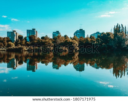 Urban landscape with green vegetation reflected in the water of a reservoir under a cloudless sigim sky.