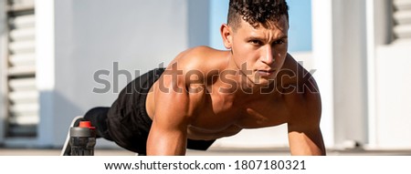Banner image of handsome muscular sports man doing plank exercise outdoors on rooftop