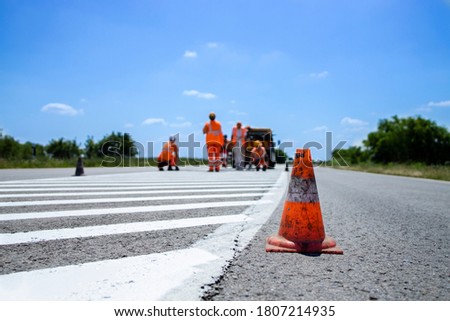 Workers in high visible suits painting lane lines on the asphalt road. Road maintenance and line visibility.