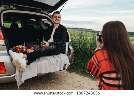 Young Beautiful Couple Having Fun Near Car, Girl Takes Pictures of Her Boyfriend