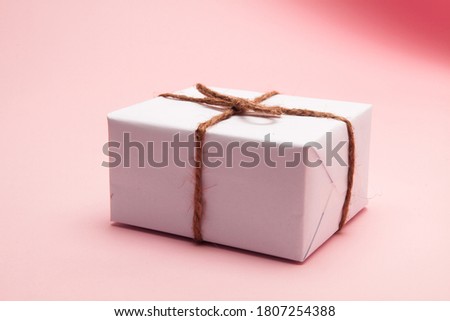 Gift box wrapped in white paper on pastel pink background 
