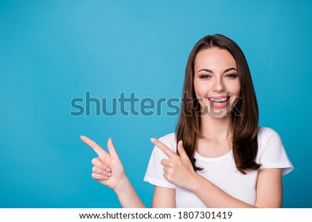 Photo of attractive pretty funny charming lady good mood directing fingers side empty space showing novelty wear casual white t-shirt isolated blue color background