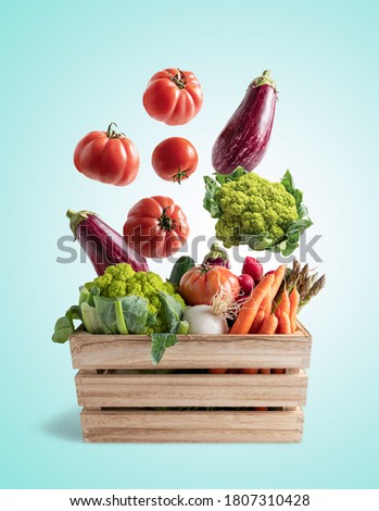 Wooden box with flying vegetables, on blue background