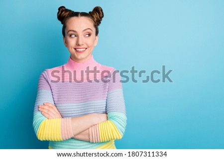 Photo of attractive teen lady two funny buns good mood toothy smile nice youngster arms crossed look side empty space interested wear casual striped sweater isolated blue color background