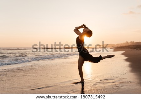 Freedom Chinese woman feeling free dancing in black elegant dress at beach sunset.