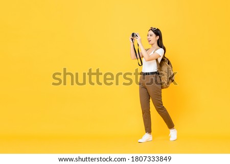 Young Asian tourist woman taking photo with camera isolated on yellow background 