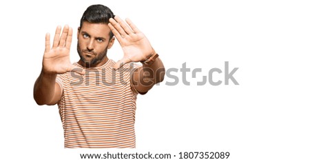 Handsome hispanic man wearing casual clothes doing frame using hands palms and fingers, camera perspective 