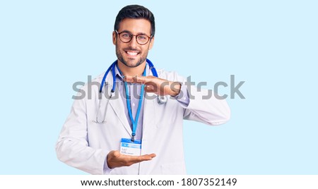 Young hispanic man wearing doctor uniform and stethoscope gesturing with hands showing big and large size sign, measure symbol. smiling looking at the camera. measuring concept. 