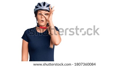 Beautiful caucasian woman wearing bike helmet doing ok gesture shocked with surprised face, eye looking through fingers. unbelieving expression. 