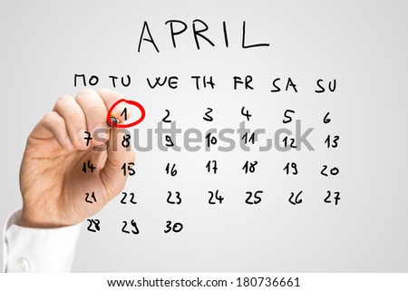 Hand drawn calendar for April on a virtual interface or screen with the First ringed in red by a man holding a marker pen, closeup of his hand. Fools day concept. Royalty-Free Stock Photo #180736661