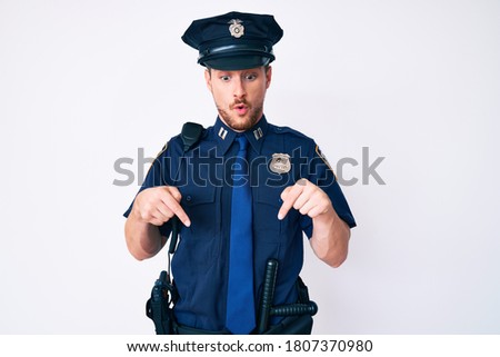 Young caucasian man wearing police uniform pointing down with fingers showing advertisement, surprised face and open mouth 