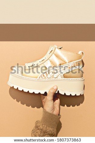 Woman Hands hold 
winter shoes on beige background.  Autumn Winter sneakers fashion concept, Fall winter season. Beige brown warm mood. Stylish strong shadows minimal design