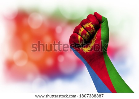 Flag of Eritrea painted on male fist, strength,power,concept of conflict. On a blurred background.
