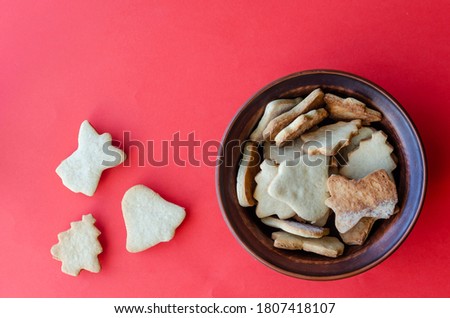 Brown clay bowl with delicious homemade Christmas cookies on red background. Traditional holiday baked goods. Copy space. View from above