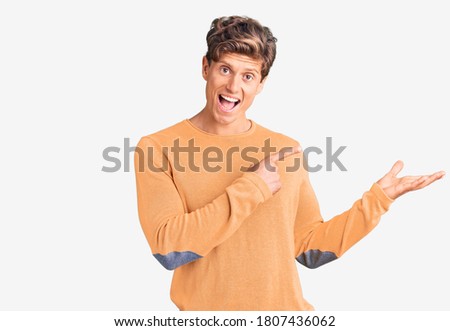 Young handsome man wearing casual clothes amazed and smiling to the camera while presenting with hand and pointing with finger. 