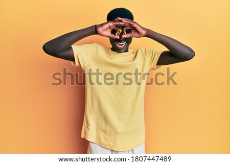 Young african american man wearing casual clothes and glasses doing ok gesture like binoculars sticking tongue out, eyes looking through fingers. crazy expression. 