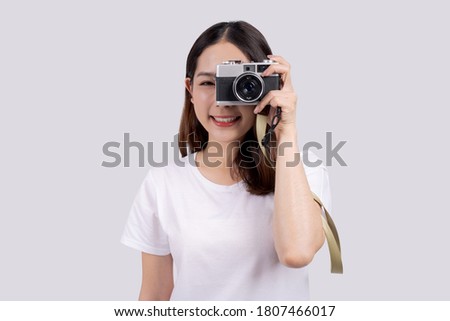 Asian woman wearing a white T-shirt is taking a picture with a camera.