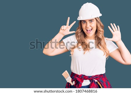 Young caucasian woman wearing security helmet showing and pointing up with fingers number eight while smiling confident and happy. 