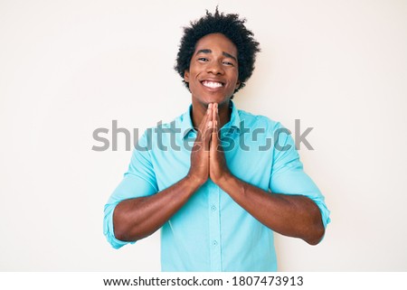 Handsome african american man with afro hair wearing casual clothes praying with hands together asking for forgiveness smiling confident. 