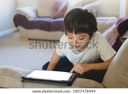 Kid pointing finger on Mock up tablet screen,Child boy lying on sofa relaxing at home watching cartoons or playing games on digital pad, Home schooling, Social Distance, E-learning online education