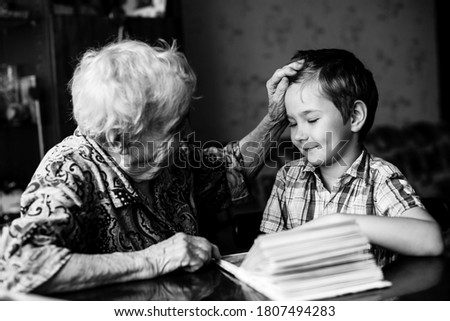 An old woman sits with his young grandson with book. Black and white photography.