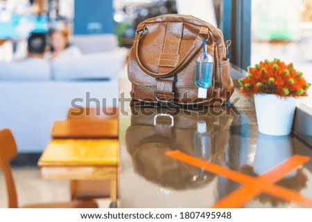 Mini portable alcohol gel bottle to kill Corona Virus(Covid-19) hang on a brown leather shoulder bag on counter in coffee shop.New normal lifestyle. Health care concept. Selective focus on alcohol gel