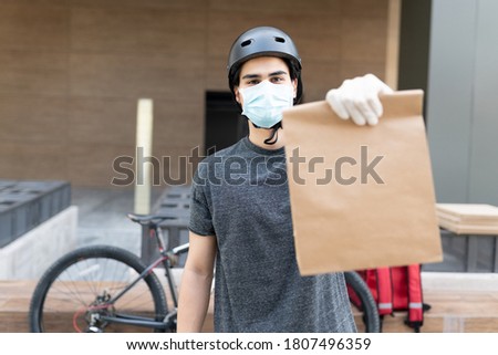 Delivery man in face mask showing parcel while standing in city during coronavirus crisis