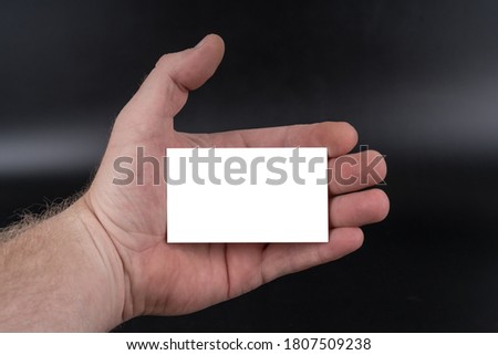 Business card in hand of businessman on black background. Blank white mock up for advertising design. Close-up