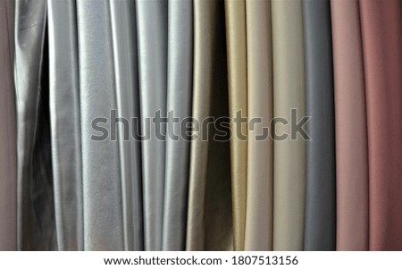 A photo of mixed shiny metallic colors leather fabrics on display. Beige, grey, charcoal, dark pink