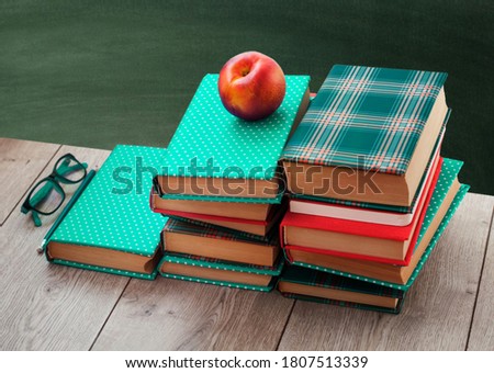Back to school, pile of books in colorful covers and peach on wooden table with empty green school board background. Distance home education.Quarantine concept of stay home