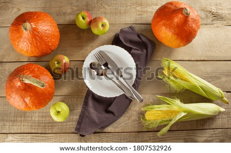Happy Thanksgiving with pumpkins and leaves, fruits and vegetables on a dark wooden background. Plate and cutlery in the center of the background.