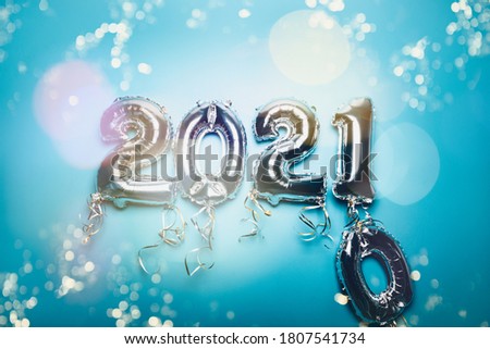 Cnanging of Year 2020 to New Year 2021 made from Silver Number Balloons. Holiday Party Decoration or postcard concept with xmas lights, on blue background