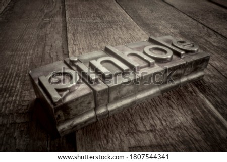 pinhole word in gritty letterpress metal type over weathered wood, soft focus image shot with lensless pinhole camera