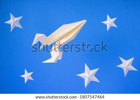 Paper origami rocket flies among paper stars on a blue background. Space concept. International Day of Human Space Flight, Cosmonautics Day.