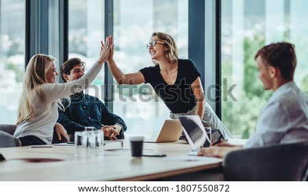 Female professional giving a high five to her colleague in conference room. Group of colleagues celebrating success in a meeting. Royalty-Free Stock Photo #1807550872