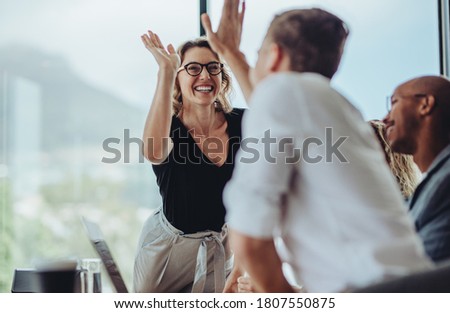 Businesswoman giving a high five to male colleague in meeting. Business professionals high five during a meeting in boardroom. Royalty-Free Stock Photo #1807550875