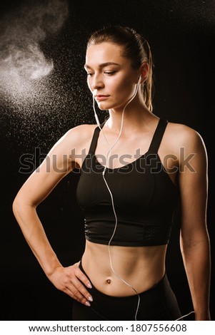 Slim sports woman with earphones on the black studio background