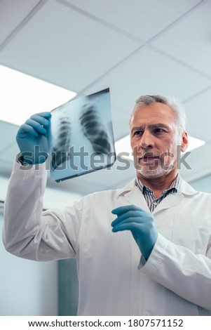 Clever Caucasian doctor putting the diagnosis while looking attentively at the chest x-ray picture