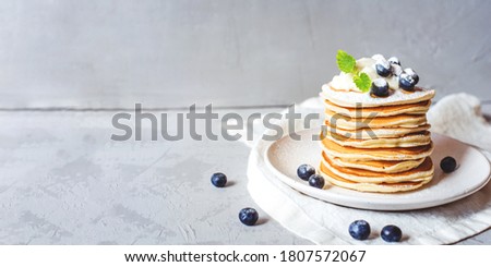 A stack of pancakes with fresh blueberries, buttercream and powdered sugar. Banner with copy space.