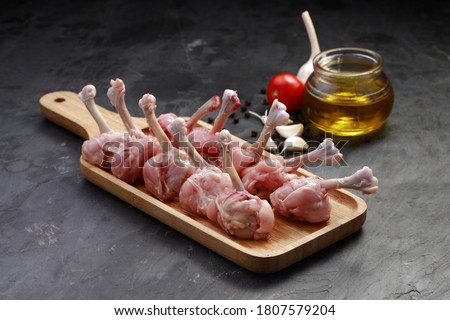 Raw chicken lollipop,ten pieces of chicken lollipop arranged on a serving board with oil, tomato and garlic on background with grey textured base Royalty-Free Stock Photo #1807579204