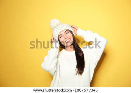 Happy young woman wearing warm sweater and knitted hat on yellow background