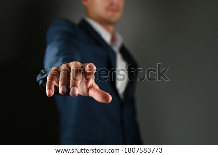 The man holds his index finger in front of him. A man in a suit points a finger forward on a black background. Concept: click on the button, specify specify.