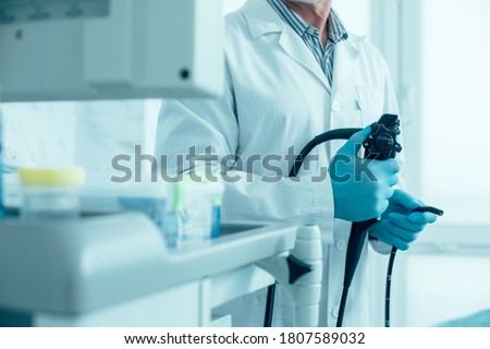 Cropped photo of a man in white coat and rubber gloves standing with a modern endoscope Royalty-Free Stock Photo #1807589032