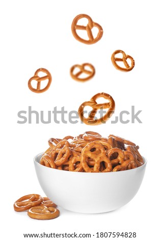 Tasty crispy pretzel crackers falling into bowl on white background Royalty-Free Stock Photo #1807594828