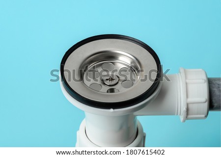 Close-up of strainer on new water trap or sink drain on a blue background. Install, clean and repair of domestic plumbing fixtures made of white pvc plastic and stainless steel. Studio shot. 