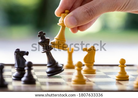 Checkmate. A man's hand is hitting the king with the queen in a chess game. Concept for playing chess outdoor, end of the game, end of the match, business strategy.  Royalty-Free Stock Photo #1807633336