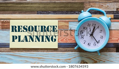Alarm clock and note sticker on desk with text Resource planning. Time management concept