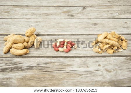 On a wooden table are three small piles of peeled peanuts, shells, whole peanuts. View from the side