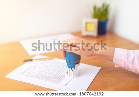 close up woman hand hold blue stamp while signing and stamping contract, make investment, taking insurance, writing will testament, office table close up